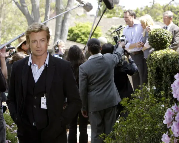 Simon Baker, con la sua nuova fidanzata, è circondato da telecamere e microfoni durante un evento all'aperto.