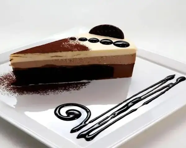 Una rebanada de tarta de tres chocolates, con capas de mousse de chocolate blanco, con leche y negro, espolvoreada con cacao y decorada con chocolate.