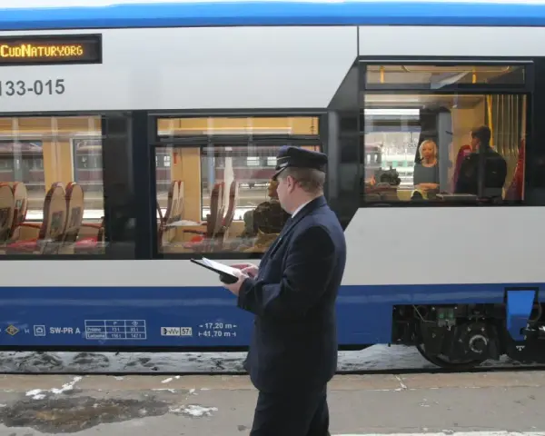 Konduktor sprawdza dane na tablecie. Zastanawiasz się, ile kosztuje bilet u konduktora? Wnętrze pociągu z siedzeniami.