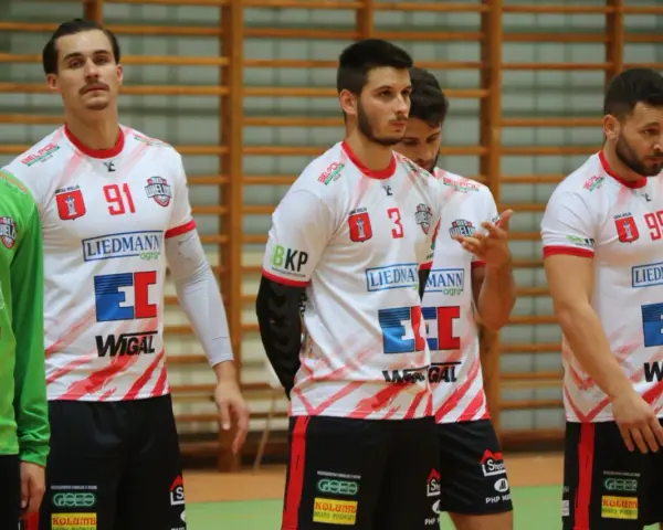 Szymon Kucharski i koledzy z drużyny w białych strojach z czerwonymi detalami, gotowi do gry.