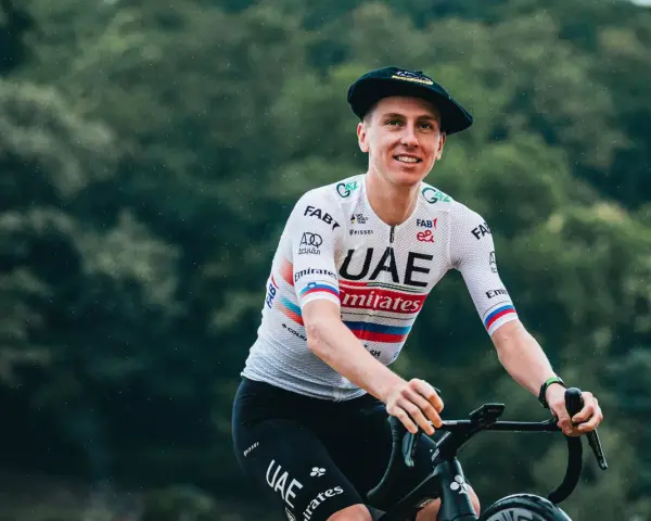 Tadej Pogačar, known for his incredible VO2 max, smiles while riding his bike in a UAE Emirates jersey and a Basque beret.