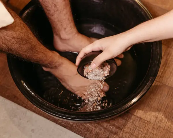 A hand pours pink salt into a foot bath, a natural substitute for Epsom salt to soak tired feet.