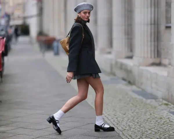 Dziewczyna w stylu Marry Jane, w szarej beretce i krótkiej spódniczce, idzie ulicą.