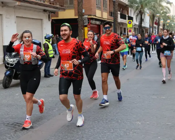 Corredores alegres participan en una media maratón, con dorsales visibles. El ambiente festivo sugiere un evento deportivo emocionante, parte de un calendario de medias maratones.