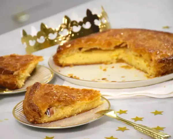 Une galette de farine dorée, prête à être dégustée, avec une fève cachée dans une part. Une couronne dorée trône à côté, promesse de fête.