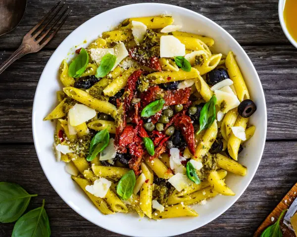 Penne con pesto, pomodori secchi, olive nere, capperi e scaglie di parmigiano. Un piatto colorato e saporito.