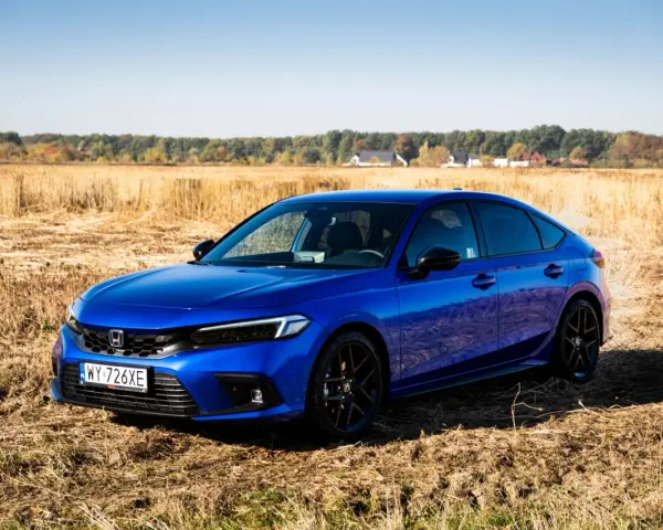 Błękitny Honda Civic 11. generacji na tle jesiennego pola.