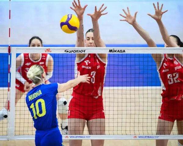 Piłka leci nad siatką podczas meczu liga światowa w piłce siatkowej. Zawodniczki w czerwonych strojach próbują ją zablokować.