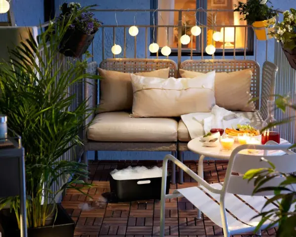 Przytulny mały balkon w bloku, z wygodną kanapą, stolikiem z przekąskami i świecami, ozdobiony lampkami i roślinami.