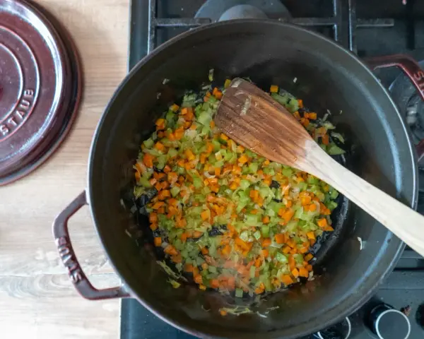 Würfel aus Karotten, Sellerie und Zwiebeln werden in einem Topf für ein soffritto rezept angedünstet.