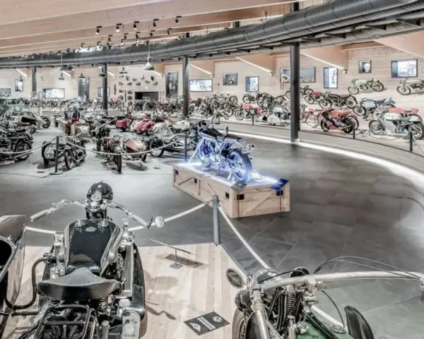 Wnętrze muzeum motocykli pełne zabytkowych maszyn, w tym motocykli z wózkami bocznymi i klasycznych samochodów.
