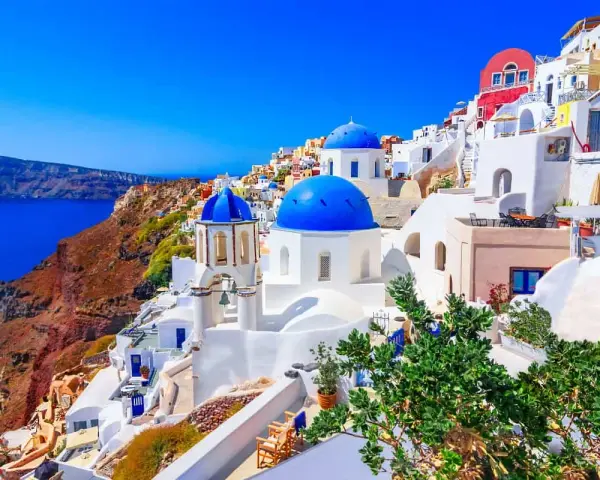 Santorini wakacje: białe domy z niebieskimi kopułami na zboczu klifu nad lazurowym morzem. Idealne miejsce na wymarzone wakacje.