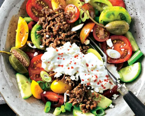 Bunter Tomatensalat mit Feta, Hackfleisch und Kapern. Frische Tomaten, Gurken und Frühlingszwiebeln bilden die Basis für diesen herzhaften Salat.