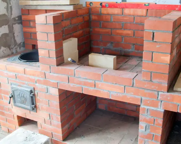 Budowa solidnego grill z cegły klinkierowej. Widać palenisko i drzwiczki.