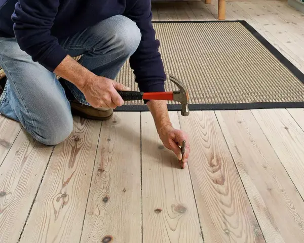 Man slår i en spik för att fixa ett knarrande golv av träplankor.