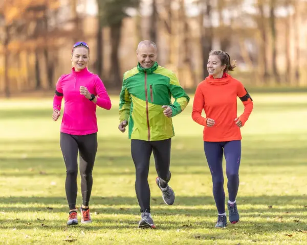 Un gruppo di amici sorridenti segue un programma allenamento corsa e camminata in un parco autunnale.