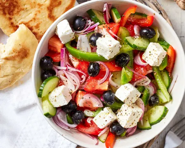 Frischer griechischer Salat mit Tomaten, Gurken, roten Zwiebeln, Oliven und Feta-Käse, serviert mit Fladenbrot.