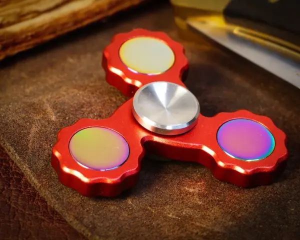 Röd fidget spinner med regnbågseffekter på de tre yttre delarna.