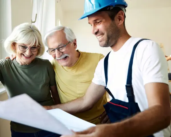 Pareja mayor sonríe mientras revisa planos con un constructor. Posibles bonificaciones mayores 65 años para su proyecto.