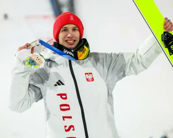 Kacper Tomasiak, skoczek narciarski, z dumą prezentuje medal i narty.