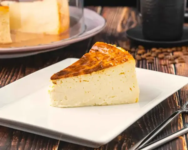 Rebanada de tarta italiana mascarpone con corteza dorada, servida en plato blanco con cubiertos.