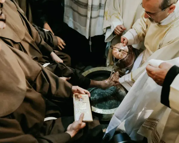 During a holy Thursday Catholic homily, a priest washes the feet of a man in a basin, symbolizing Christ's humility.