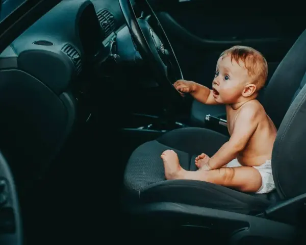 Maluch w pieluszce siedzi za kierownicą, jakby zastanawiał się, od kiedy dziecko może jeździć z przodu.