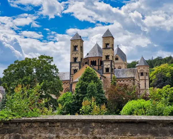 A grand Romanesque abbey, where Benedictine monks lived, stands amidst lush greenery under a dramatic sky.