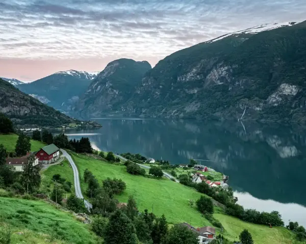 Grönskande bergssluttningar med hus vid en fjord i Norge. Perfekt för att planera dina inreseregler Norge.