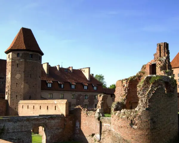 Potężne zamki nad morzem bałtyckim, w tym ruiny i zachowane budowle z cegły, pod błękitnym niebem.