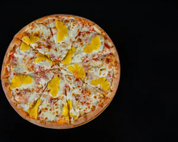 Pizza hawajska z kurczakiem i ananasem na czarnym tle.