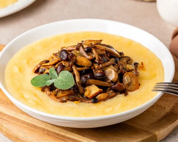 Polenta cremosa con champiñones salteados y una ramita de salvia. Un plato reconfortante que te hará preguntar: ¿polenta que es? ¡Deliciosa!