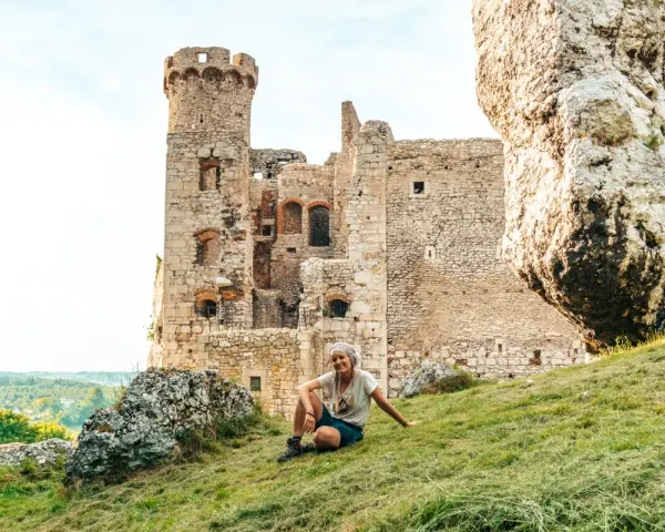 Kobieta odpoczywa na trawie przed ruinami zamku na Szlaku Orlich Gniazd. Ile zamków czeka na odkrycie?