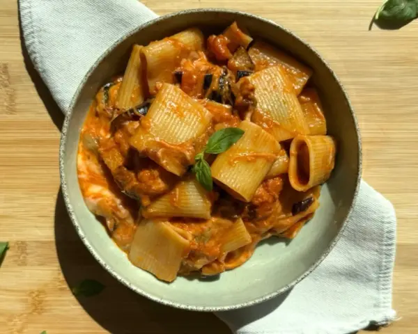 Piatto di pasta alla siciliana con rigatoni, melanzane e pomodoro, guarnito con basilico fresco.
