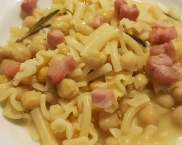 Piatto di pasta e ceci in scatola, con cubetti di pancetta e un rametto di rosmarino.