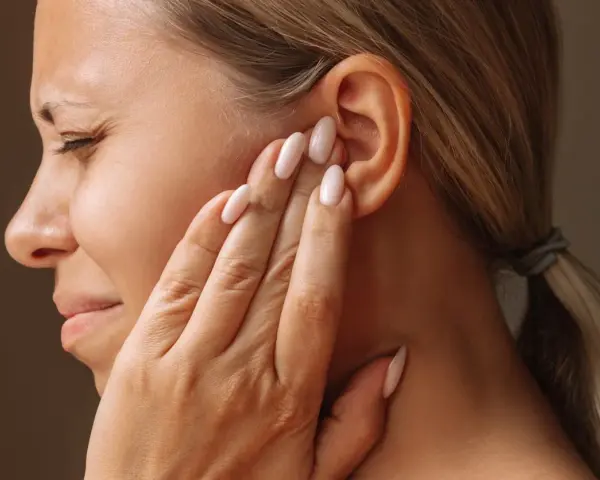 Une femme se tient l'oreille, le visage crispé, comme si elle entendait un bruit sourd dans les oreilles.