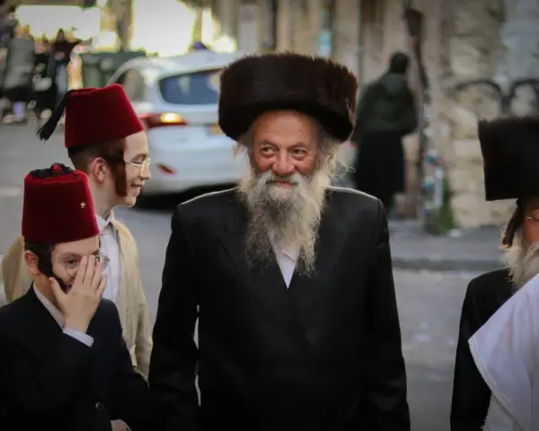 Men in traditional attire, including fur hats and red fez hats, walk together, perhaps celebrating the Purim meaning of joy and community.