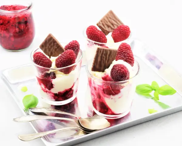 Drei Gläser mit cremigem Dessert, Himbeeren und Schokolade. Ein Glas mit Himbeermarmelade daneben. Schnelles Eis für den Sommer.
