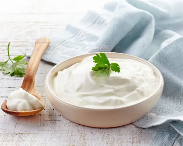 Gęsta, biała śmietana 30 kcal w miseczce, obok drewniana łyżka z porcją. Idealna do deserów i sosów.