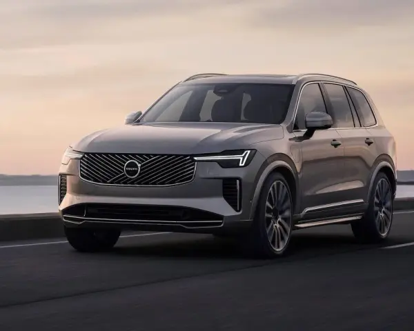 Elegancki, szary Volvo CX90 jedzie po drodze nad jeziorem o zachodzie słońca.