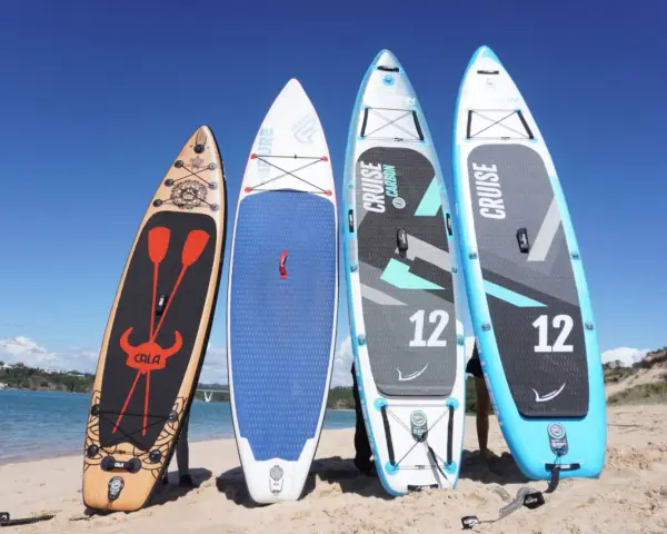 Vier Stand Up Paddles am Strand. Die Boards zeigen verschiedene Designs und Größen, die die Vor- und Nachteile von Stand up paddling beeinflussen können.