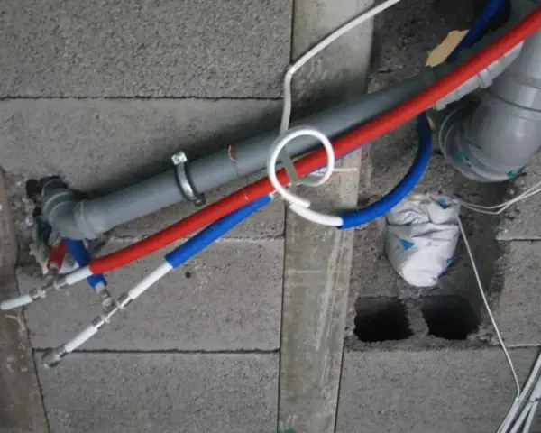Instalacja wodna z rurami PP w ścianie z pustaków. Widoczne rury czerwone i niebieskie, szary odpływ.