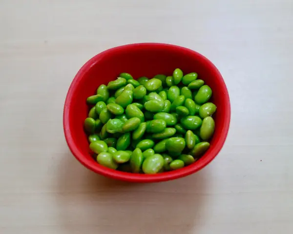 Czerwona miseczka pełna zielonych ziaren soi. Czy to edamame? Tak, to właśnie edamame, zdrowe i pyszne!