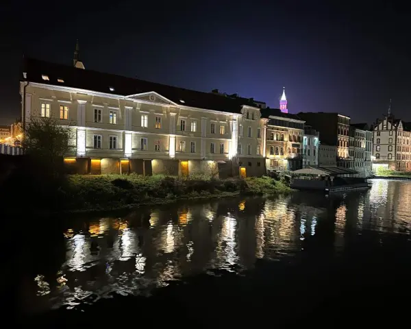 Nocna panorama miasta nad rzeką, z oświetlonymi kamienicami i odbiciami świateł w wodzie. To prawdziwa opolska wenecja.