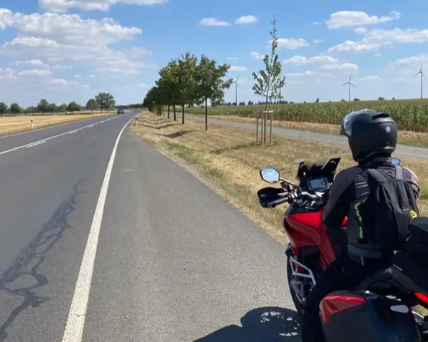 Motociclista su strada panoramica Foresta Nera, con campi di mais e pale eoliche all'orizzonte.