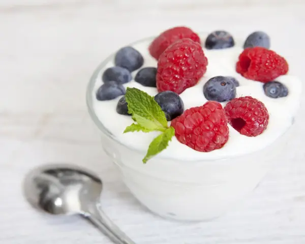 Pyszny jogurt z malinami i borówkami, idealny na śniadanie lub jako element diety jogurtowej. Obok leży łyżeczka.