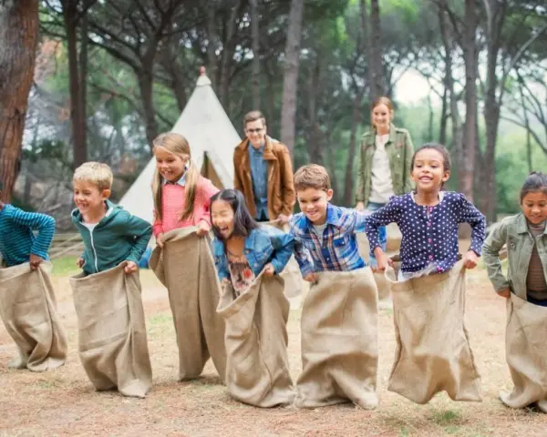 Des enfants participent à une course en sac dans un camp de vacances en forêt.