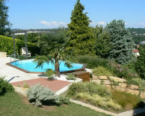 Piscine aux formes douces sur un terrain en pente, entourée de végétation luxuriante et d'une terrasse en bois.