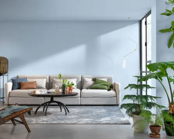 Jasny salon z wygodną kanapą, stolikiem kawowym i dużą ilością roślin. Sufit w kolorze ścian tworzy spójną, spokojną atmosferę.