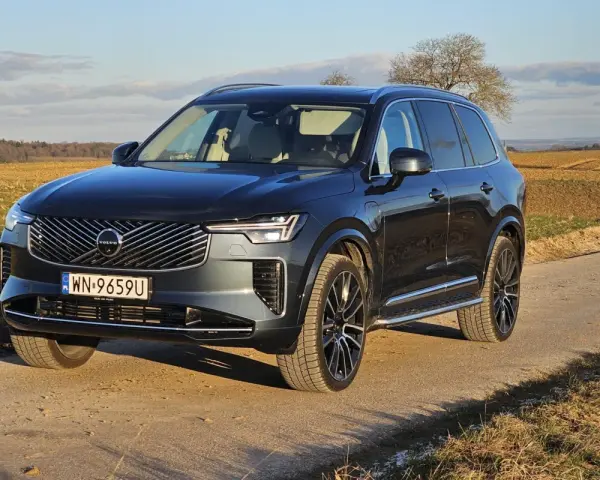 Ciemnoszary Volvo XC90 T8 na tle jesiennego krajobrazu. Elegancki SUV z nowoczesnym grillem i światłami LED.